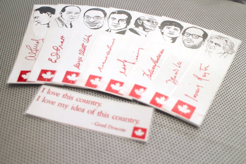 May include: A collection of white bookmarks with red maple leaf designs and black and white illustrations of famous Canadians. The bookmarks feature the signatures of the individuals pictured. The text "I love this country. I love my idea of this country." is printed on a separate bookmark.