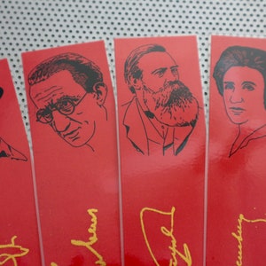 May include: Five red bookmarks with black and white illustrations of famous people. Each bookmark has a gold signature at the bottom.