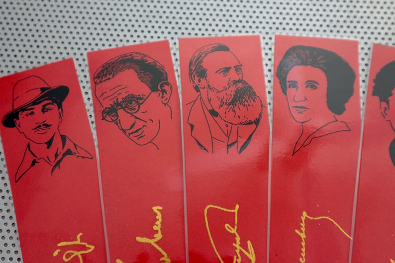 May include: Five red bookmarks with black and white illustrations of famous people. Each bookmark has a gold signature at the bottom.