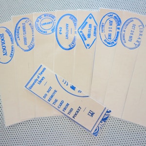 Puede incluir: Una colección de tarjetas y bolsillos de biblioteca antiguos. Las tarjetas son de color beige con sellos de tinta azul de varios departamentos y fechas. Un bolsillo dice: "NO RETIRE LA TARJETA DE ESTE BOLSILLO".