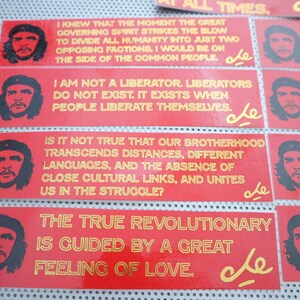 May include: A collection of red and gold stickers with quotes from Che Guevara. The stickers feature a portrait of Che Guevara and the text "Che" in gold lettering. The quotes include "I knew that the moment the great governing spirit strikes the blow to divide all humanity into just two opposing factions, I would be on the side of the common people."