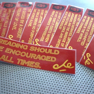 May include: A stack of red and gold bookmarks with inspirational quotes. The top bookmark reads "Reading should be encouraged at all times."