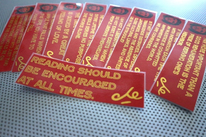 May include: A stack of red and gold bookmarks with inspirational quotes. The top bookmark reads "Reading should be encouraged at all times."