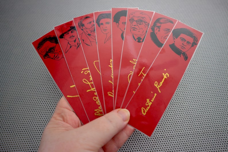 May include: Set of eight red bookmarks with black and white illustrations of famous authors. Each bookmark features a gold signature of the author, including "J.K. Rowling", "Maya Angelou", "Neil Gaiman", "Stephen King", "Jane Austen", "Charles Dickens", "Virginia Woolf", and "Ernest Hemingway".