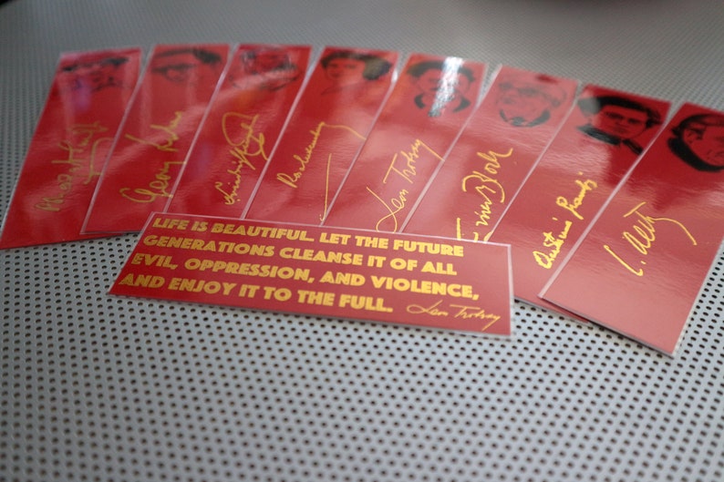 May include: A set of red bookmarks with gold lettering and images of people. The bookmarks feature quotes from famous people, including "Life is beautiful. Let the future generations cleanse it of all evil, oppression, and violence, and enjoy it to the full." - Leon Trotsky.