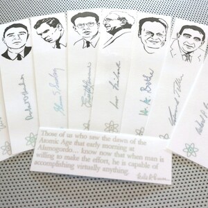 Op de afbeelding: Een set van acht zwart-witte bladwijzers met portretten van wetenschappers met hun handtekeningen. De bladwijzers zijn gedrukt op wit papier met een citaat over de dageraad van het atoomtijdperk.