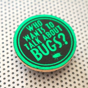May include: A round, green and black button with the text "Who wants to talk about bugs?" in white lettering. A small black silhouette of a bug is below the text.