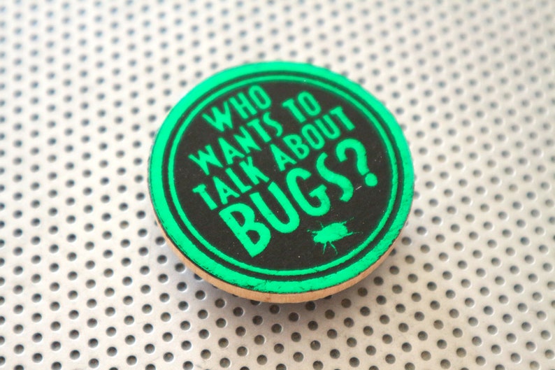 May include: A round, green and black button with the text "Who wants to talk about bugs?" in white lettering. A small black silhouette of a bug is below the text.