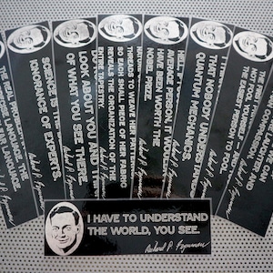 May include: Black bookmarks with quotes by Richard Feynman. Each bookmark features a portrait of Feynman and a quote in white text. A rectangular bookmark at the bottom also has a quote.