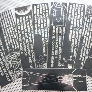May include: A set of black and white bookmarks with quotes about astronomy and space. The bookmarks feature illustrations of planets, stars, and celestial bodies. The quotes include: "To confine our attention to terrestrial matters would to limit the human spirit." - Stephen Hawking, "Space won't believe how big it really is." - Douglas Adams, "Look at the stars! Look at all the fire-folk sitting in the air! The bright boroughs, the oriole-ontalds there." - Gerard Manley Hopkins, "Astronomy is the civil division of time, the soul of chronology and geography, and the only guide of the navigator." - Nicolas Louis de Lacaille, "If you are cheerful, and wide, go leave the study of astronomy alone. Of all the sciences, it alone deserves the character of the terrible." - Thomas Hardy.