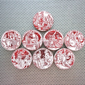 May include: Eight round ceramic tiles with red and white illustrations of people in various scenes. The tiles are arranged in a circle on a silver background.