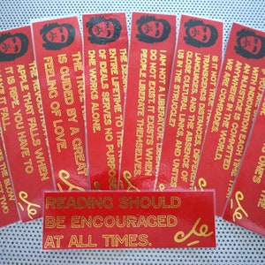 May include: A set of ten red bookmarks with gold lettering featuring quotes by Che Guevara. The bookmarks feature a stylized image of Che Guevara's face. The text on the bookmarks includes quotes such as "Far more important than a good remuneration is the pride of serving one's neighbor." and "Reading should be encouraged at all times."
