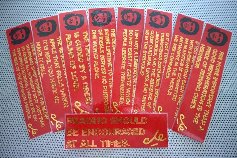 May include: A set of ten red bookmarks with gold lettering featuring quotes by Che Guevara. The bookmarks feature a stylized image of Che Guevara's face. The text on the bookmarks includes quotes such as "Far more important than a good remuneration is the pride of serving one's neighbor." and "Reading should be encouraged at all times."