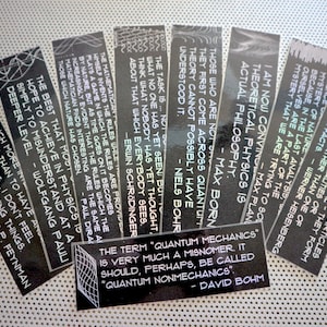 Puede incluir: Un conjunto de diez marcapáginas en blanco y negro con citas inspiradoras sobre física y ciencia. Las citas son de científicos famosos como Erwin Schrödinger, Max Planck y Niels Bohr. Los marcapáginas están impresos en un fondo negro texturizado con texto blanco.