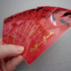 May include: A stack of red bookmarks with black and white images of famous people. The bookmarks have gold lettering that says "Austin Franks".