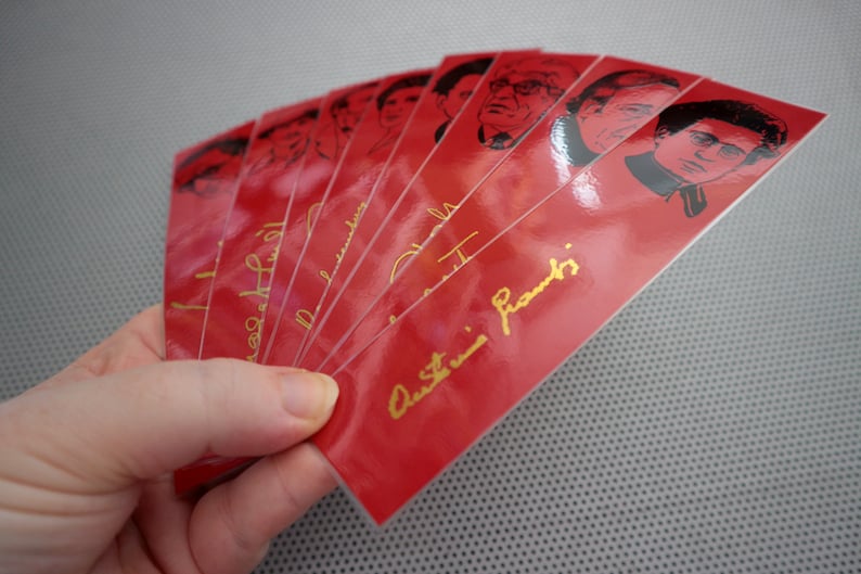 May include: A stack of red bookmarks with black and white images of famous people. The bookmarks have gold lettering that says "Austin Franks".
