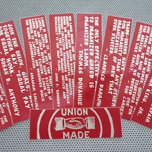 Op de afbeelding: Een verzameling rode en witte stickers met citaten over vakbonden. De stickers bevatten tekst zoals "De arbeidersbeweging was de belangrijkste kracht die ellende en wanhoop in hoop en vooruitgang veranderde." en "Sluit je aan bij de vakbond, meisjes, zeg samen: "Gelijke betaling voor gelijk werk."