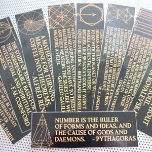 May include: A set of black and gold bookmarks with geometric designs and inspirational quotes about mathematics. The quotes include "Number is the ruler of forms and ideas, and the cause of gods and daemons. - Pythagoras" and "It is impossible to be a mathematician without being a poet in soul. - Sofia Kovalevska".