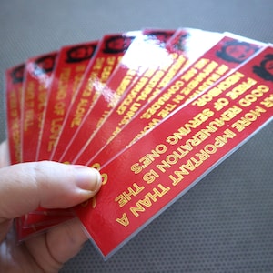 May include: A stack of red bookmarks with gold lettering. The bookmarks feature a quote from Che Guevara: "Far more important than a good remuneration is the pride of serving one's people."