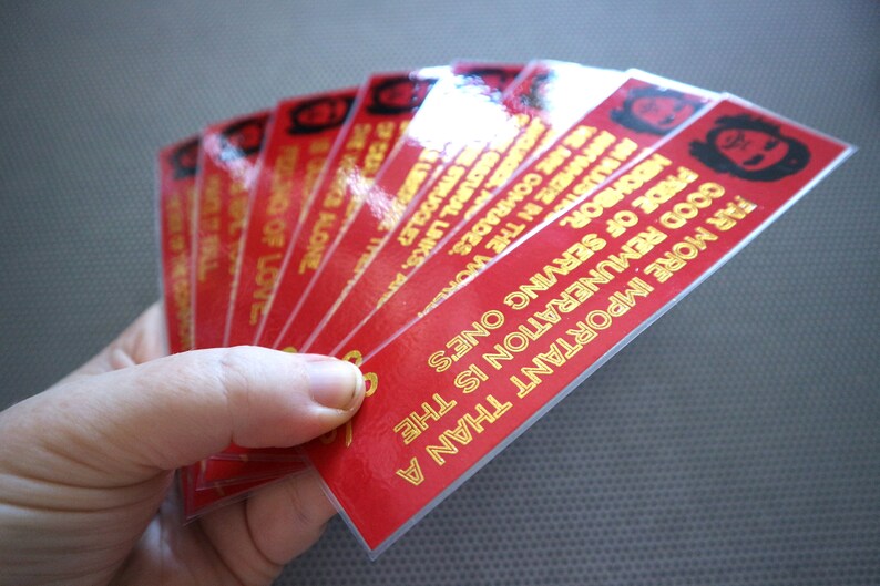 May include: A stack of red bookmarks with gold lettering. The bookmarks feature a quote from Che Guevara: "Far more important than a good remuneration is the pride of serving one's people."