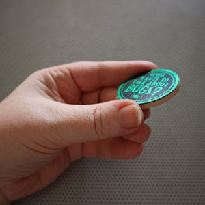 May include: A round wooden token with a black background and green text that reads "Who wants to talk about bugs?"