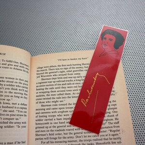 May include: A red bookmark with a gold inscription of "I'll have to harden my heart" and a portrait of a woman in black and white. The bookmark has a gold signature that reads "Pat Alexander".