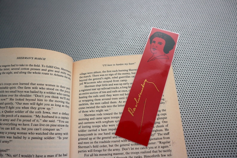 May include: A red bookmark with a gold inscription of "I'll have to harden my heart" and a portrait of a woman in black and white. The bookmark has a gold signature that reads "Pat Alexander".