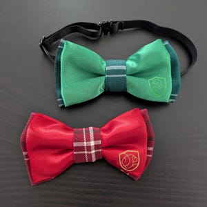 May include: Two bow ties, one green with a green snake emblem and one red with a red lion emblem.