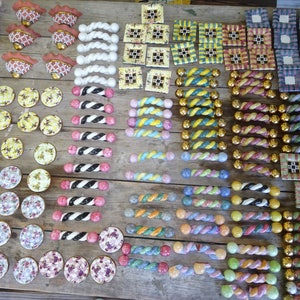 Puede incluir: Una colecci&oacute;n de pomos y tiradores decorativos de cer&aacute;mica en varios dise&ntilde;os y colores. El surtido incluye patrones florales, a rayas y geom&eacute;tricos, con detalles dorados y plateados. Los pomos y tiradores est&aacute;n dispuestos sobre una superficie de madera.