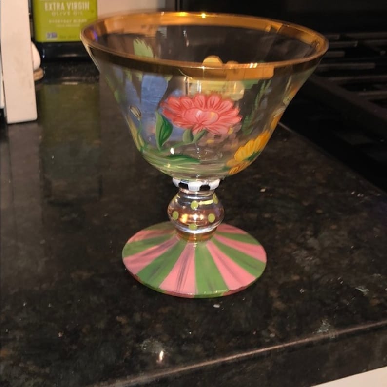 Puede incluir: Una copa de cristal transparente con borde dorado y dise&ntilde;o floral pintado. La copa presenta una base a rayas rosas y verdes y un tallo decorativo con detalles dorados. Las flores son rojas y amarillas.