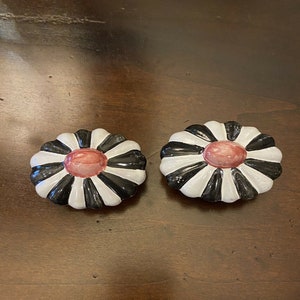 May include: Two black and white ceramic flower-shaped buttons with a red center.