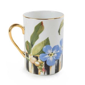 May include: A white ceramic mug with a gold rim and handle. The mug features a black and white striped pattern with blue flowers and green leaves.