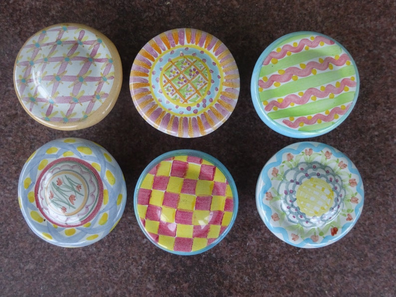 May include: Six small, hand-painted ceramic dishes with colourful, patterned designs. Each dish features a unique combination of colours and patterns, including checks, floral motifs, and geometric shapes. The dishes are arranged in a circular pattern.