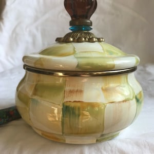 Puede incluir: Un tarro de cerámica con un patrón de cuadros verdes y blancos. La tapa tiene un pomo marrón con un acento azul.