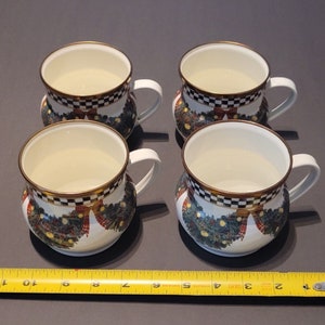 K&ouml;nnte beinhalten: Vier wei&szlig;e Keramikbecher mit goldenen R&auml;ndern und wei&szlig;en Griffen. Jeder Becher hat ein schwarz-wei&szlig; kariertes Band oben und ein festliches Kranzdesign mit roten Schleifen und gr&uuml;nem Laub. Die Becher haben einen Durchmesser von etwa 10 cm.