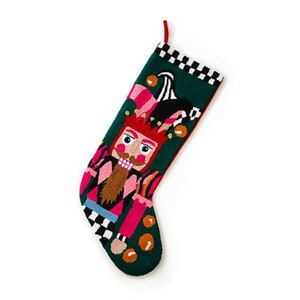 May include: A Christmas stocking with a whimsical nutcracker design. The stocking features a green background with a colorful nutcracker figure in pink, red, and brown. The top border has a black and white checkered pattern, and a red loop for hanging.