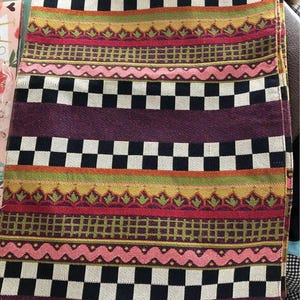 Puede incluir: Un mantel individual tejido de colores con un patrón de cuadros negros y blancos, rayas rosas y verdes y un fondo morado.