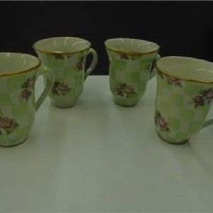 May include: Set of four green and white ceramic teacups with floral designs. The cups have a checkered pattern and are decorated with pink roses.