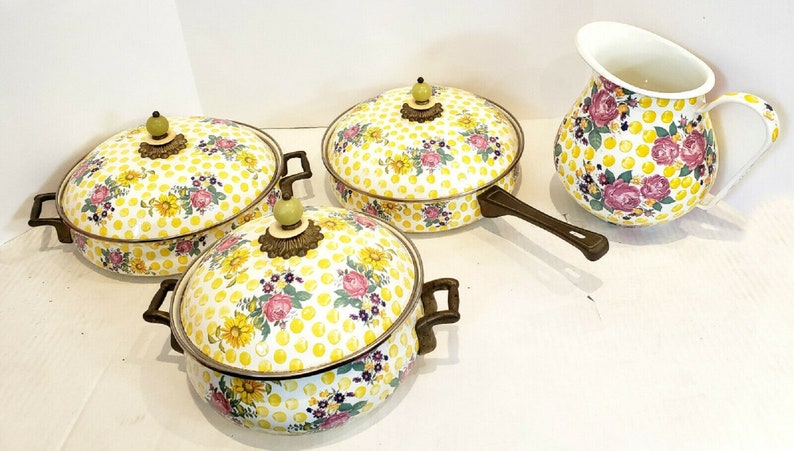 May include: A set of vintage kitchenware featuring a yellow polka dot pattern with floral accents. The set includes three lidded pots and a pitcher. The pots have brown handles and decorative brass-toned accents. The pitcher has a white interior.