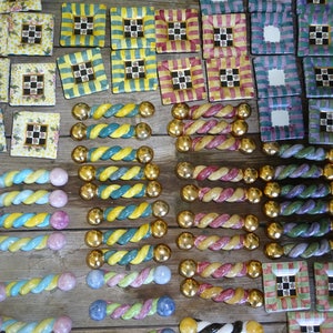 Puede incluir: Una colecci&oacute;n de coloridos pomos de cer&aacute;mica decorativos y baldosas cuadradas con varios dise&ntilde;os. Los pomos tienen un dise&ntilde;o retorcido con extremos dorados. Las baldosas presentan dise&ntilde;os florales, a cuadros y a rayas en tonos amarillos, verdes, rosas y azules.