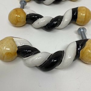 May include: Three ceramic cabinet knobs with a twisted design. The knobs are white, black, and yellow.