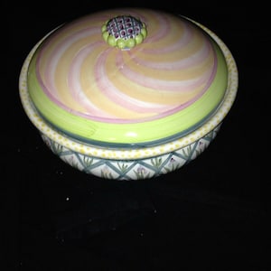 Może przedstawiać: Ceramiczna miska z pokrywką. Pokrywka ma spiralny wzór w kolorze różowym i żółtym z zieloną obwódką. Miska ma zielono-biały wzór z żółtymi kropkami.