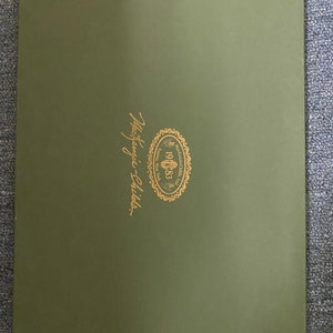 May include: A green folder with a gold logo that says "Mackenzie-Childs" and "Established 1983" with a floral design.