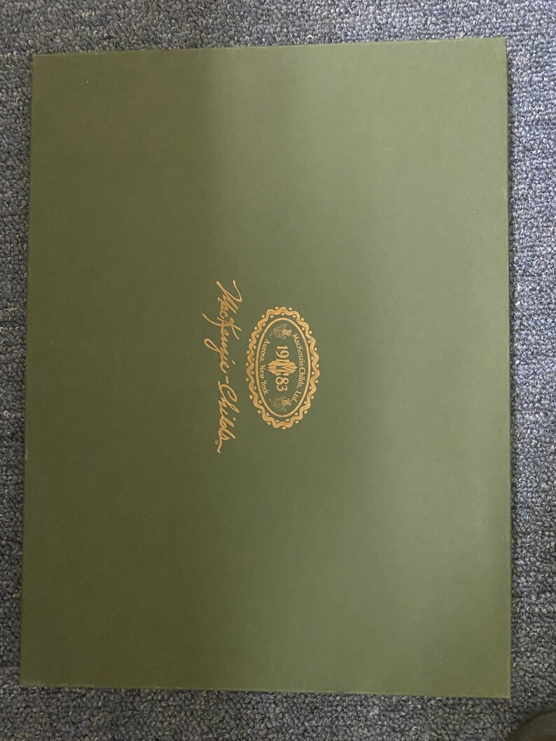 May include: A green folder with a gold logo that says "Mackenzie-Childs" and "Established 1983" with a floral design.