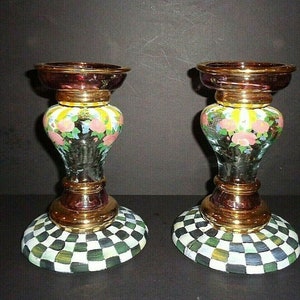 Puede incluir: Dos candelabros decorativos de cristal. Cada uno tiene una parte superior e inferior de color burdeos, con una banda dorada en el medio. La secci&oacute;n central es de cristal transparente con un dise&ntilde;o floral. La base tiene un patr&oacute;n de cuadros verdes, blancos y negros.