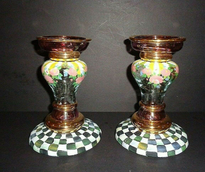 Puede incluir: Dos candelabros decorativos de cristal. Cada uno tiene una parte superior e inferior de color burdeos, con una banda dorada en el medio. La secci&oacute;n central es de cristal transparente con un dise&ntilde;o floral. La base tiene un patr&oacute;n de cuadros verdes, blancos y negros.