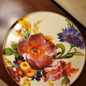 Op de afbeelding: Een ronde witte serveerschaal met een bloemenontwerp met paarse, gele en blauwe bloemen. De schaal heeft een gouden rand.