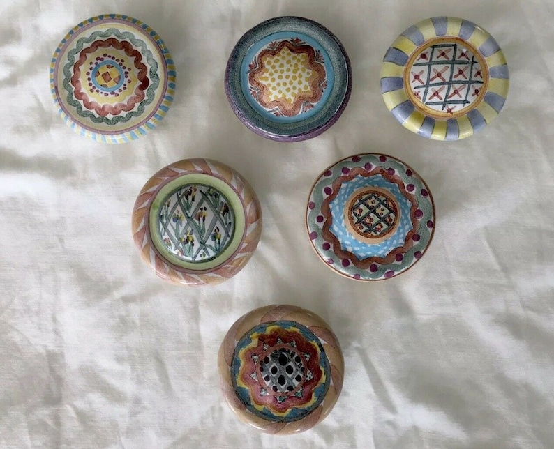 May include: Six decorative ceramic knobs with detailed patterns. The knobs display various designs, including floral and geometric patterns, in colours such as blue, yellow, red, and green. Each round knob has a unique, hand-painted appearance. Measurements are in centimetres.