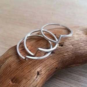 Peut inclure: Trois bagues en argent avec un design géométrique. Les bagues sont empilées les unes sur les autres et reposent sur une surface en bois.