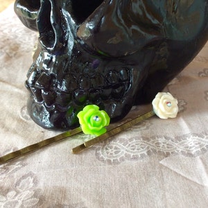 May include: Two gold hair clips with decorative flower accents. One flower is green with a rhinestone center, and the other is white with a rhinestone center.